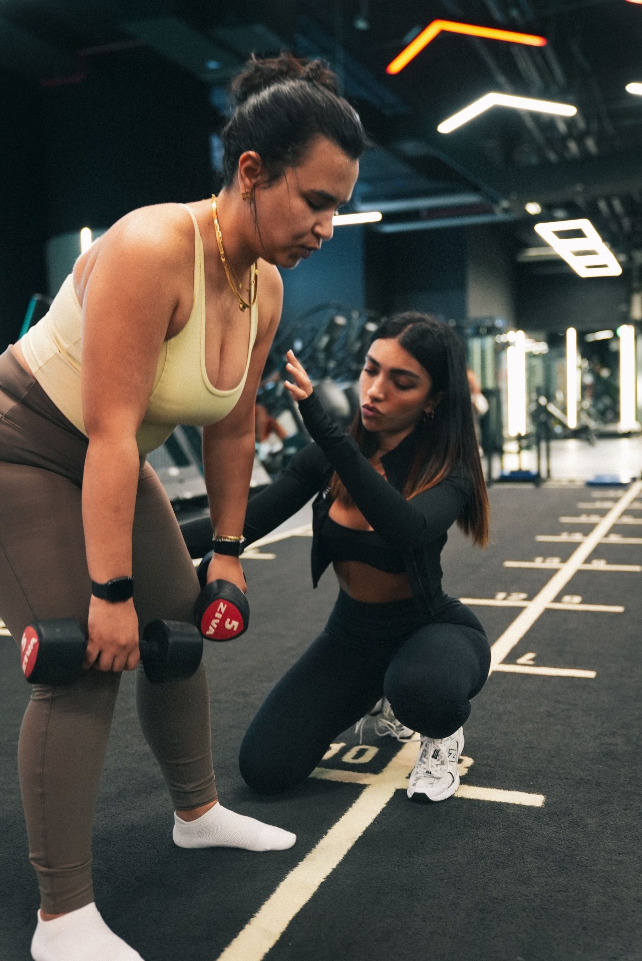 Project Reshape coach kneeling to cue a client through a dumbbell row