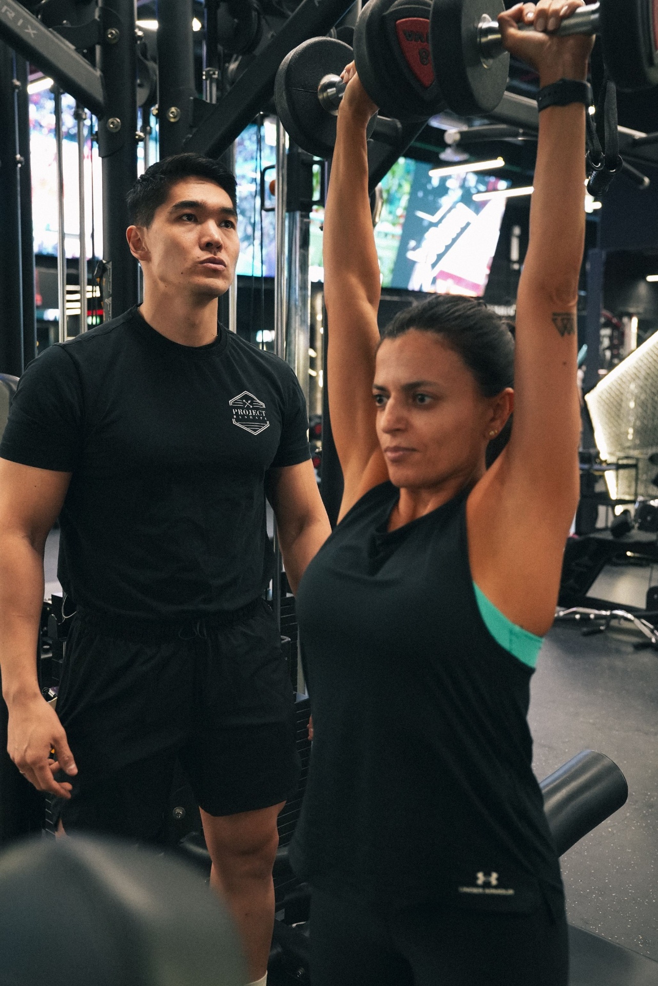 Project Reshape coach observing a client press dumbbells overhead